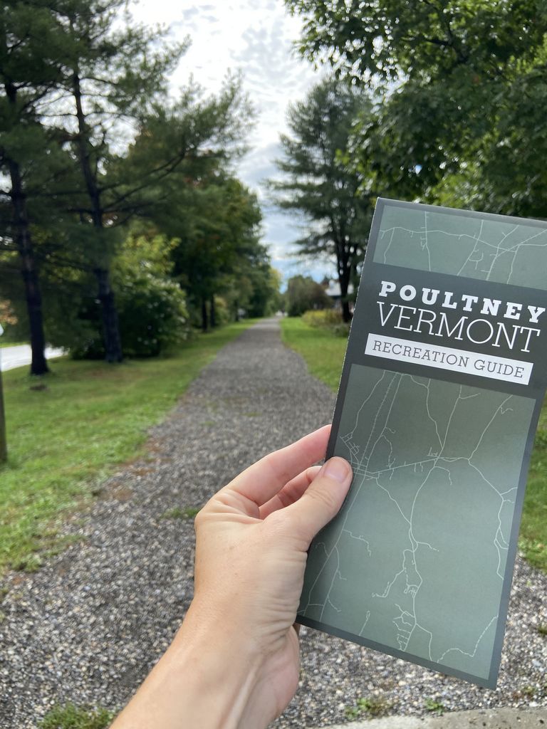 Person holding the Poultney Recreation brochure next to the D&H Rail Trail Person holding the Poultney Recreation brochure next to the D&H Rail Trail